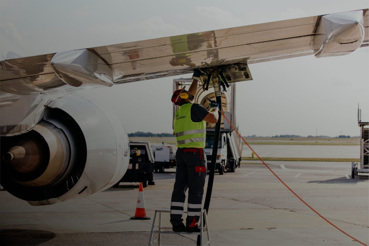 Mężczyzna ubrany w odzież ochronną napełnia zbiornik samolotu paliwem lotniczym na płycie lotniska.  