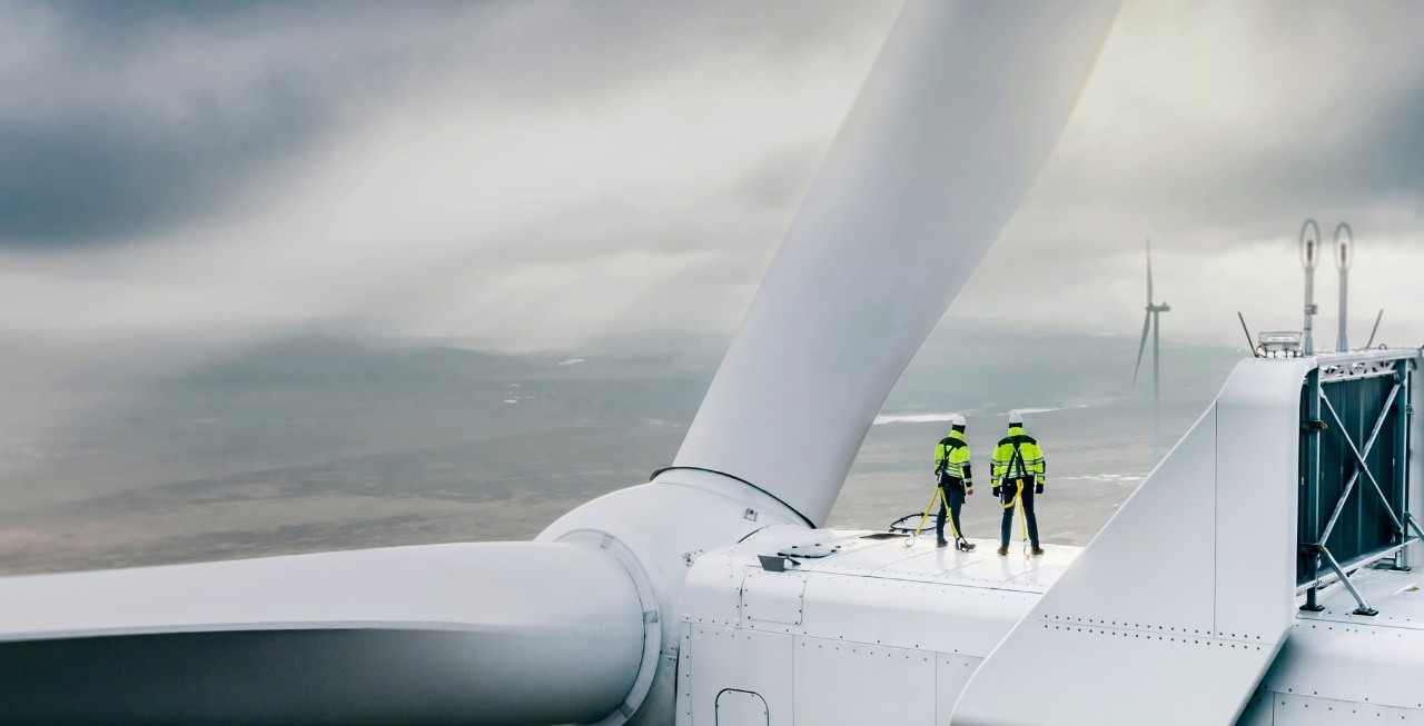 Wiatraki i OZE ORLEN. Dwoje ludzi w ubraniach roboczych i kaskach ochronnych, stojących na górnej części turbiny wiatrowej. 