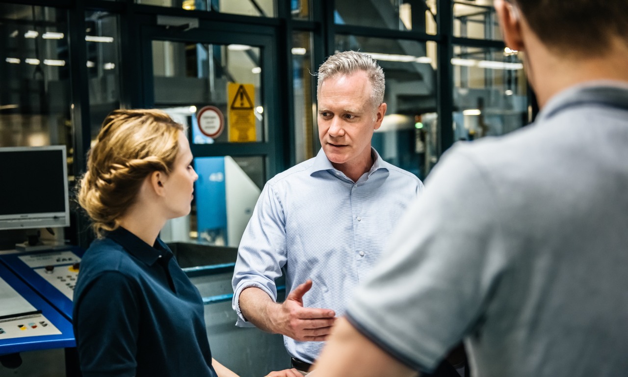 Manager, engineer and trainee talking during a meeting close to a production line in a printery