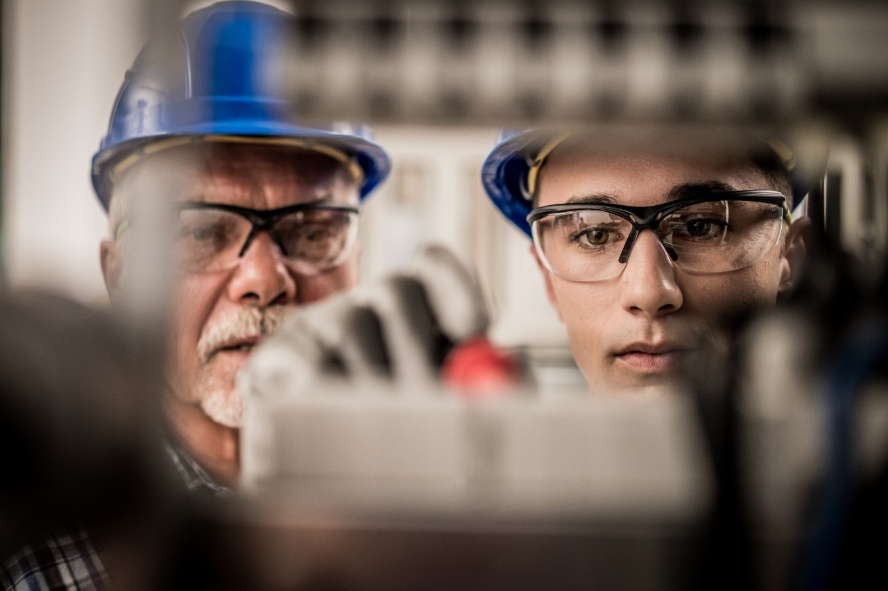 Close up of male apprentice connecting the wires in the distribution board under supervision of a senior electrician.