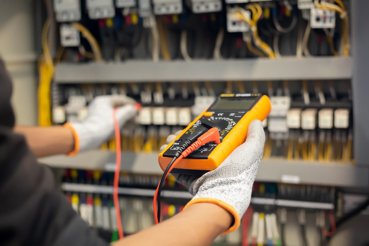 Electrician engineer uses a multimeter to test the electrical installation and power line current in an electrical system control cabinet.