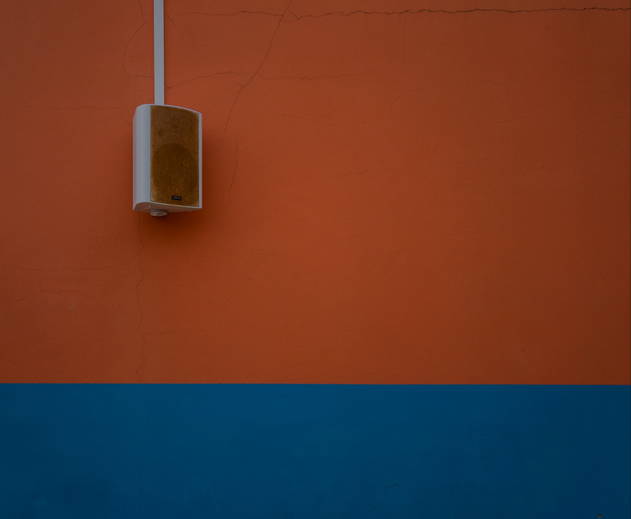 Głośnik zawieszony na pomarańczowo-granatowej ścianie budynku.  
