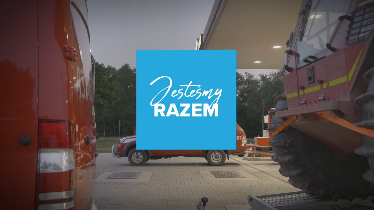 Elektromobilność i stacje ładowania pojazdów elektrycznych– Grupa ORLEN. Samochód elektryczny zaparkowany przy stacji ładowania, z widocznym kablem ładowania podłączonym do gniazda w pojeździe. 
