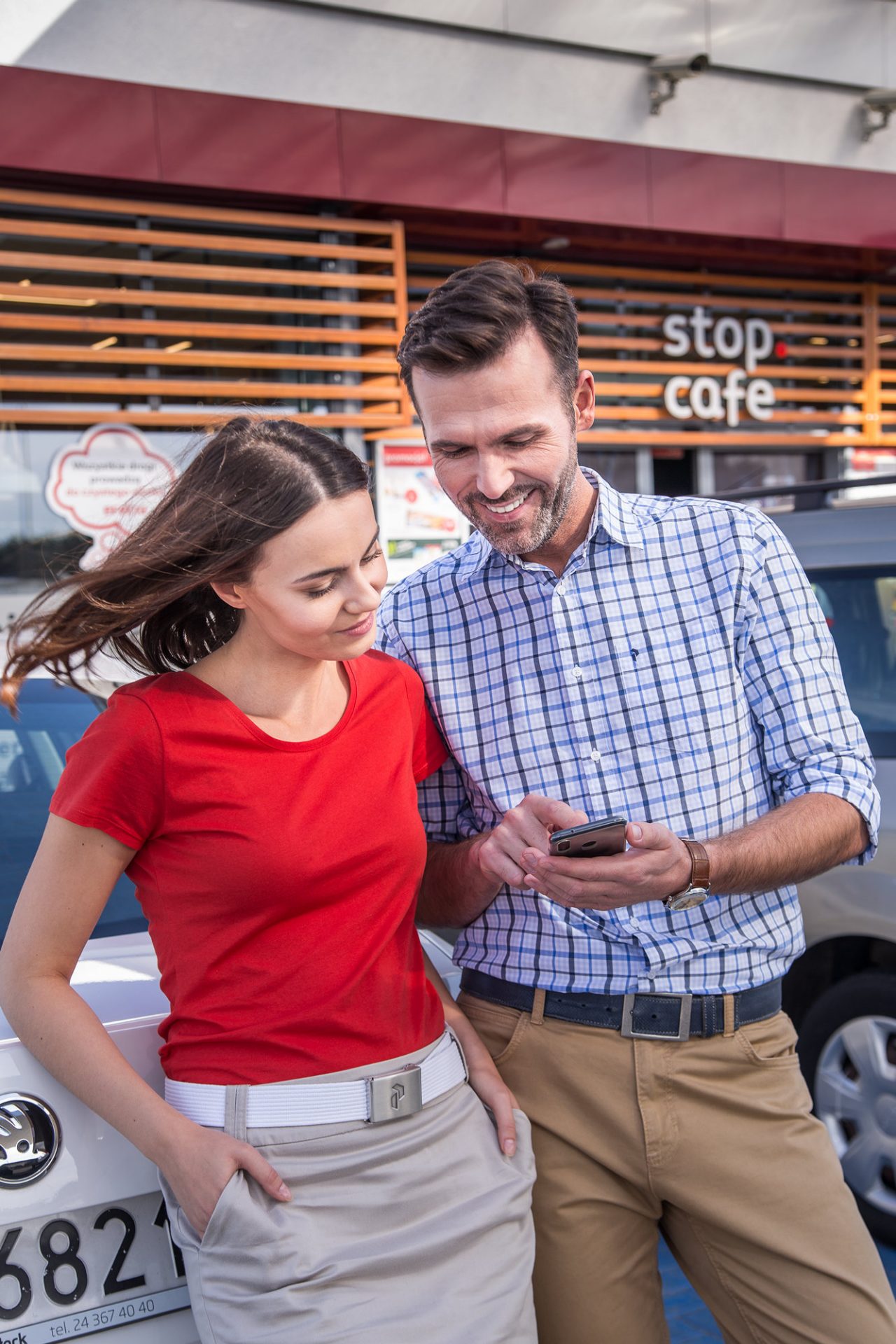 Aplikacja ORLEN VITAY. Kobieta i mężczyzna rozmawiają na parkingu samochodowym pod punktem Stop Cafe. 