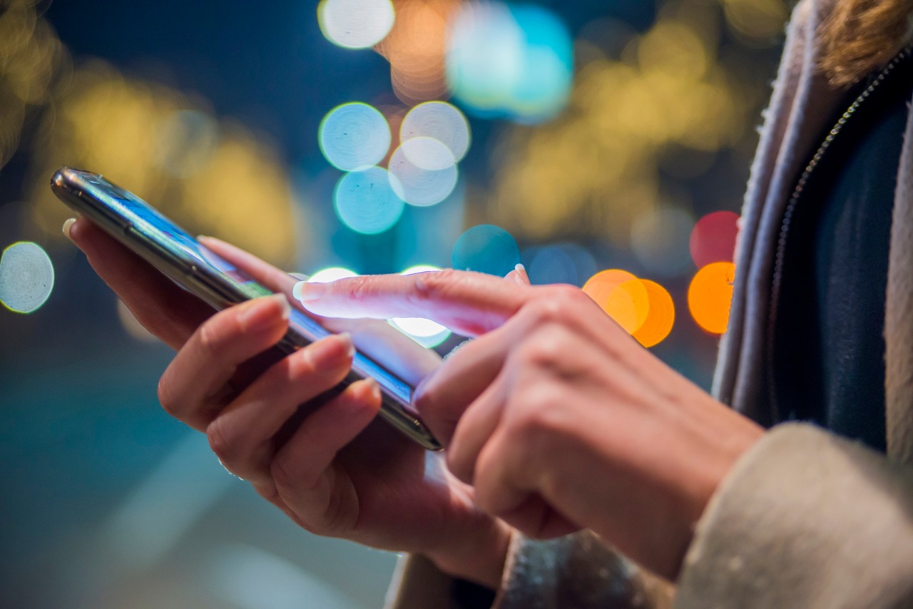 ORLEN innowacje. Kobieta trzyma w dłoniach telefon komórkowy i przegląda wiadomości lub próbuje wykonać połączenie.