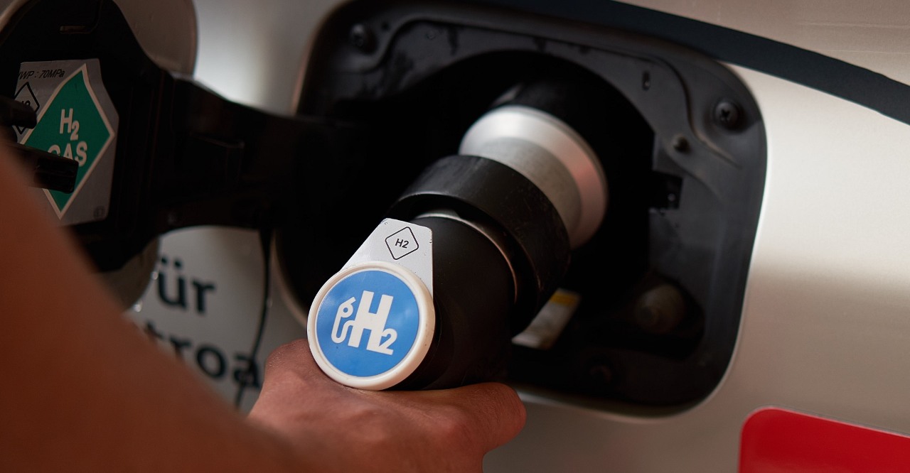 Wodór H2 i paliwo wodorowe – Grupa ORLEN.  Ręka osoby tankującej paliwo wodorowe, trzymająca wąż dystrybutora umieszczony we wlewie paliwa pojazdu zasilanego wodorem.