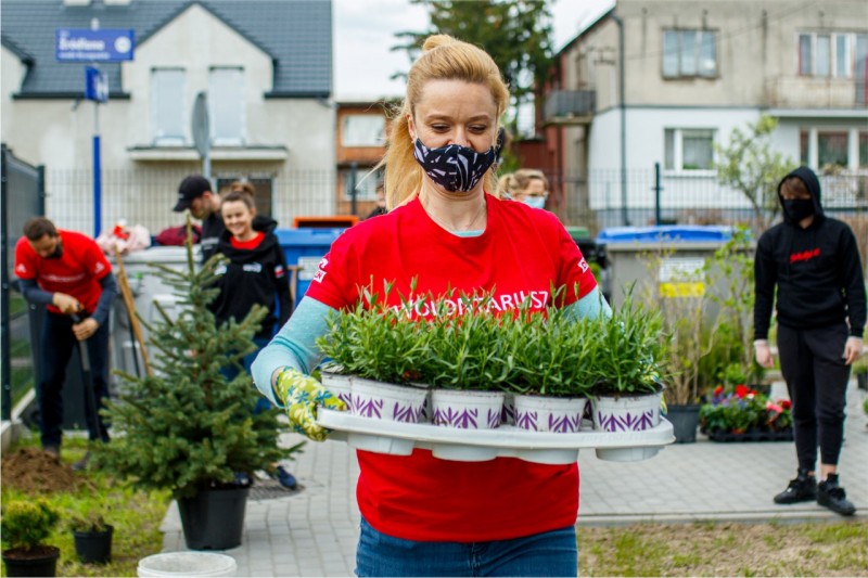 ESG ORLEN i ekologia. ORLEN Fundacja. Wolontariuszka niesie doniczki z roślinami. Inni wolontariusze sadzą rośliny aby wpierać ekologiczne inicjatywy i dbać o środowisko. 