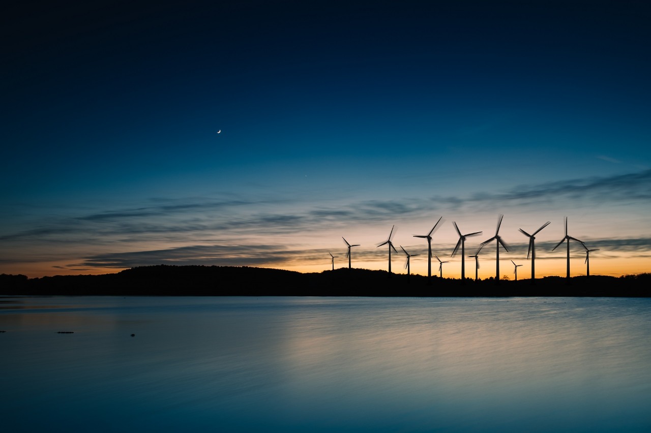 OZE ORLEN. Rząd wiatraków na tle zachodzącego słońca symbolizujących ekologiczną produkcję energii.