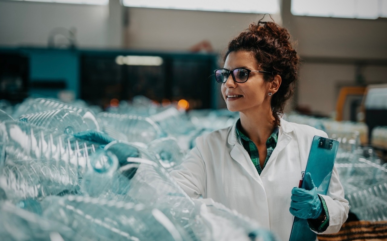 GOZ i inwestycje – Grupa ORLEN. Kobieta stoi na tle wielu plastikowych butelek w zakładzie recyklingu, pracując nad procesem przetwarzania odpadów i ochroną środowiska.